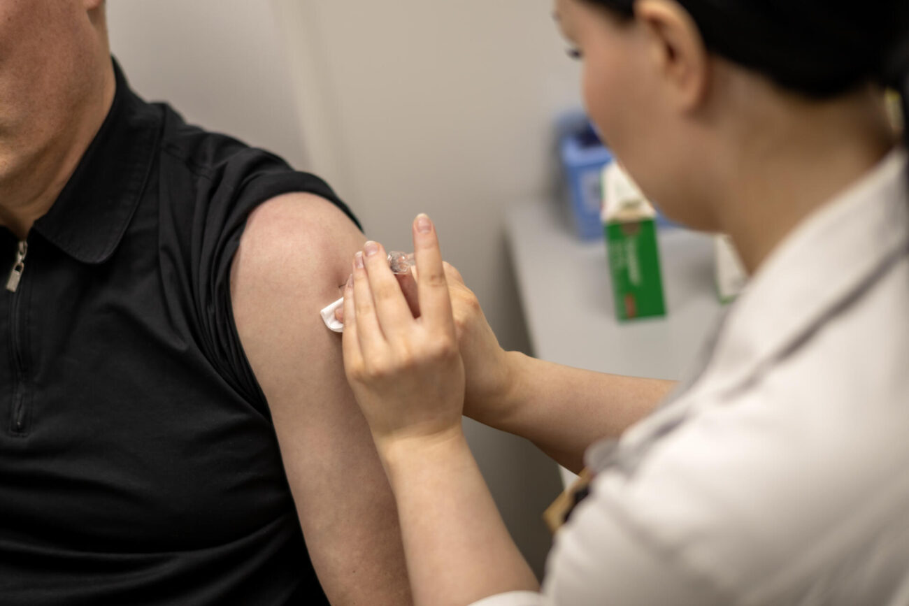 Farmaseutti Jenna Ukkonen pistää rokotteen Antti Mäntylän käsivarteen.