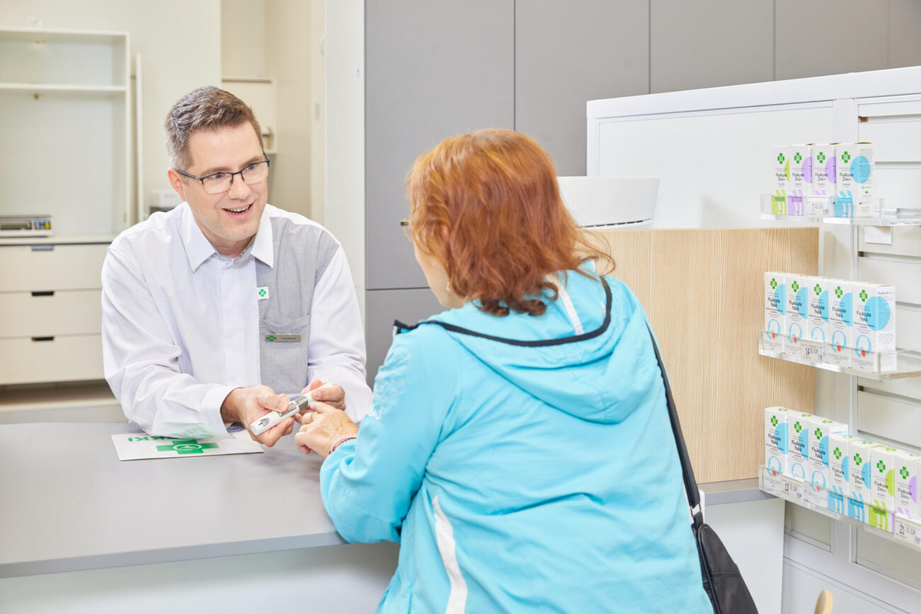 Farmaseutti neuvoo apteekin asiakkaalle biologisen lääkkeen antolaitteen käyttöä.