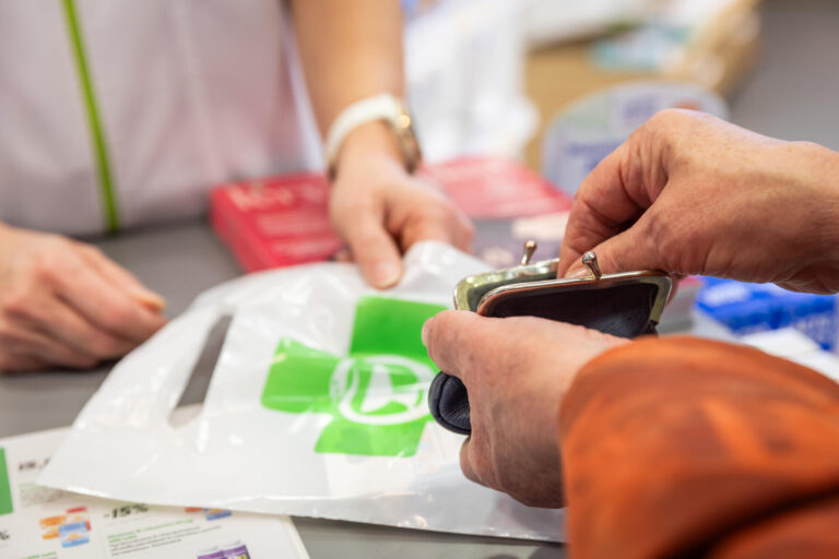 Lähikuva, jossa apteekin asiakas kaivaa kukkarostaan kolikoita lääkkeiden maksamiseen,