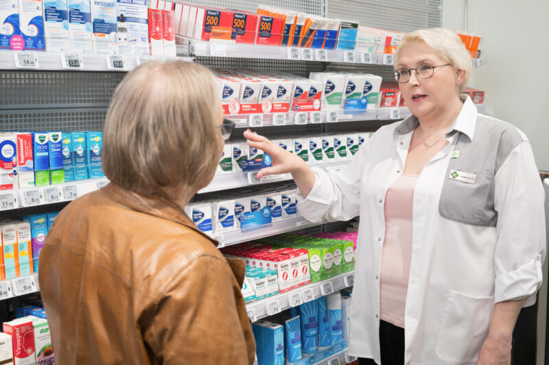 Farmaseutti ja asiakas apteekin itsehoitolääkehyllyn edessä.