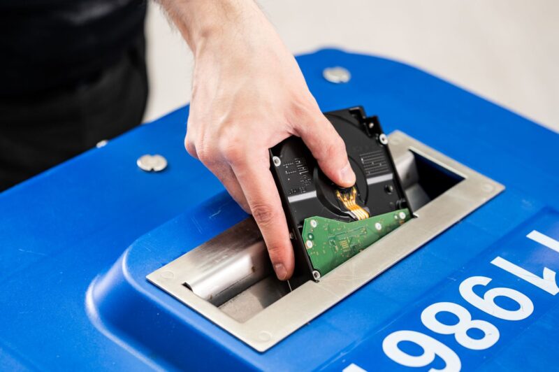 Lähikuva, jossa joku laittaa materiaalia turvaroskiksen luukusta sisään.