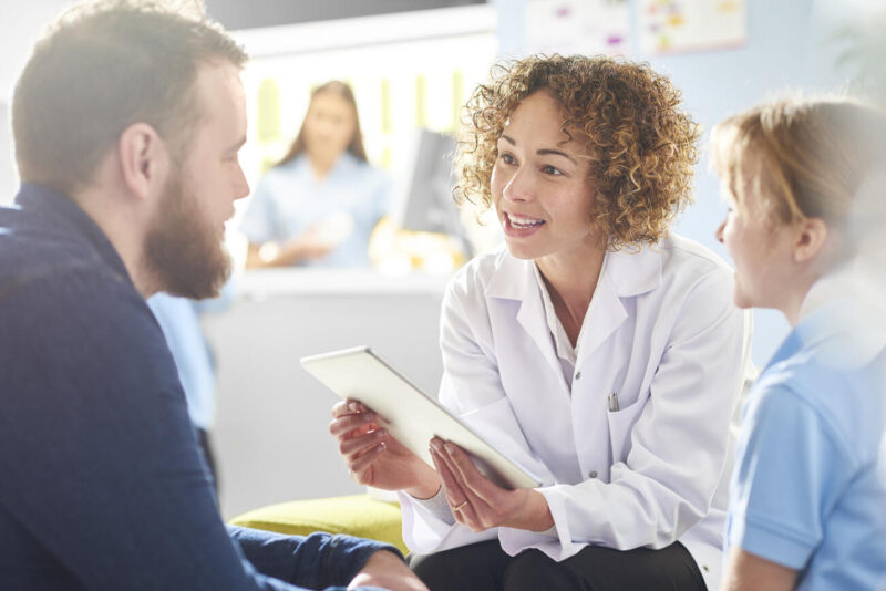 ISTOCK A female pharmacist sits with a father and sick daughter in the pharmacist consultation area and discusses his prescription and choice of medication viewing the details on a digital tablet. In the background a senior woman and is at the counter being served by a female pharmacy assistant .