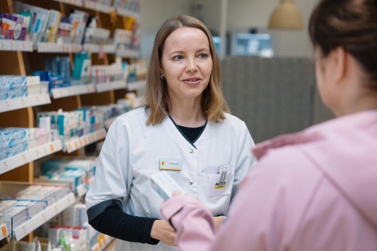Apteekkari Hanna Ylä-Rautio juttelee asiakkaan kanssa itsehoitolääkehyllyn luona.