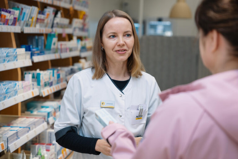 Apteekkari Hanna Ylä-Rautio juttelee asiakkaan kanssa itsehoitolääkehyllyn luona.